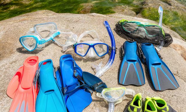 Family snorkel sets, masks, fins, and water shoes arranged near a coastal inlet